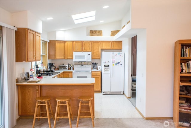 kitchen with white appliances, lofted ceiling with skylight, a peninsula, a sink, and recessed lighting