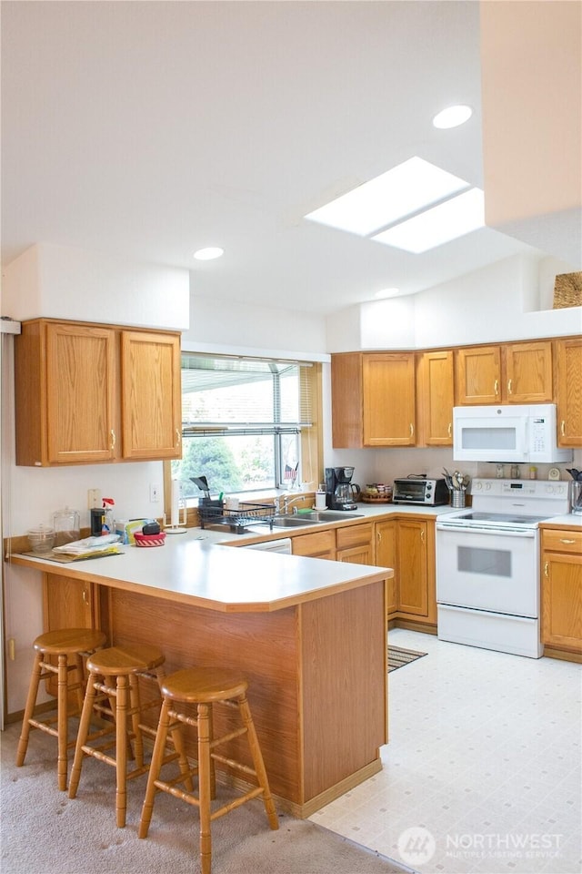 kitchen with a breakfast bar area, recessed lighting, light countertops, white appliances, and a peninsula