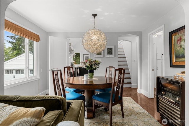 dining area featuring wood finished floors, baseboards, arched walkways, stairs, and a notable chandelier