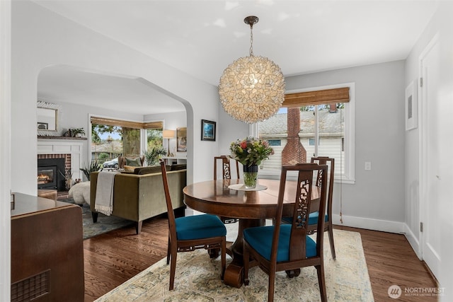 dining room featuring a brick fireplace, wood finished floors, arched walkways, and a wealth of natural light