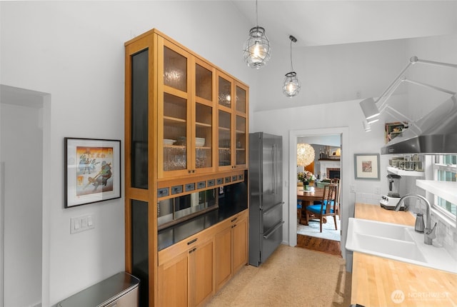 kitchen featuring pendant lighting, a sink, high quality fridge, glass insert cabinets, and vaulted ceiling