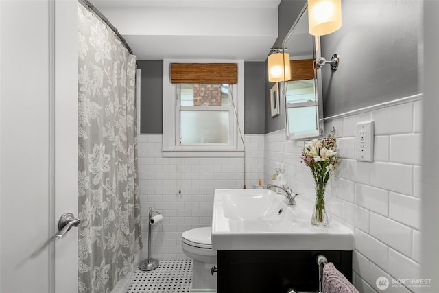 full bath featuring toilet, a shower with shower curtain, vanity, wainscoting, and tile walls