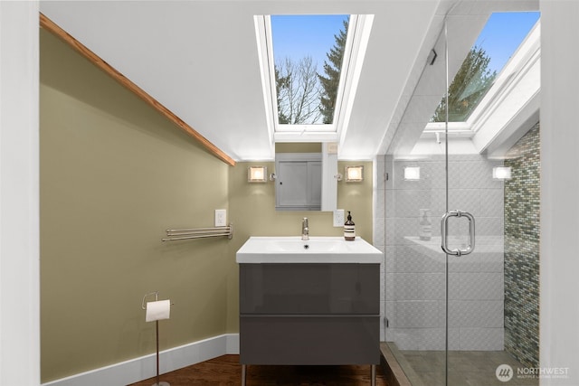 full bathroom with vanity, wood finished floors, baseboards, a skylight, and a stall shower