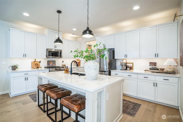 kitchen with stainless steel appliances, white cabinetry, an island with sink, and light hardwood / wood-style flooring