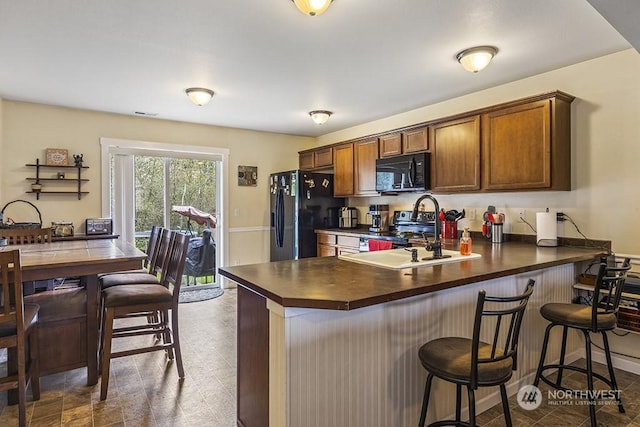 kitchen featuring sink, black appliances, a kitchen breakfast bar, and kitchen peninsula