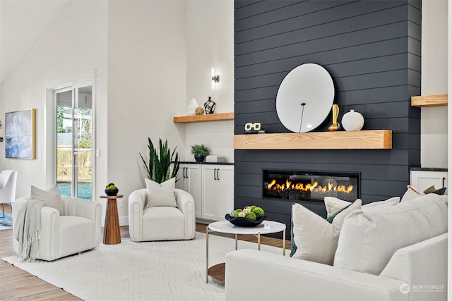 living room with a large fireplace, vaulted ceiling, wooden walls, and light hardwood / wood-style floors