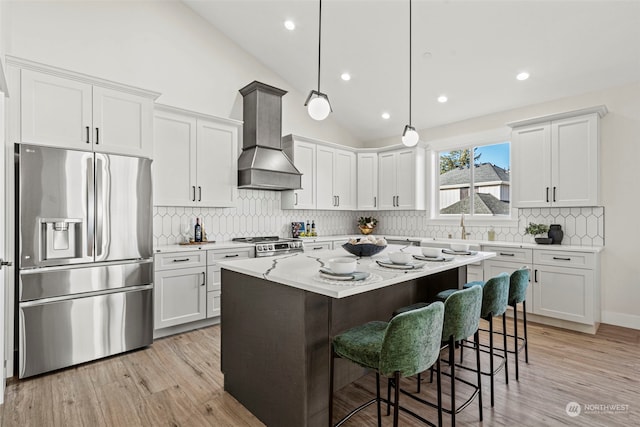 kitchen with a center island, appliances with stainless steel finishes, premium range hood, white cabinetry, and hanging light fixtures