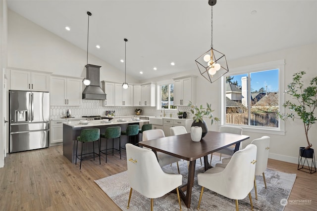 dining room with light hardwood / wood-style floors, sink, and high vaulted ceiling