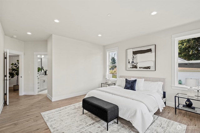 bedroom featuring connected bathroom, light hardwood / wood-style flooring, and multiple windows