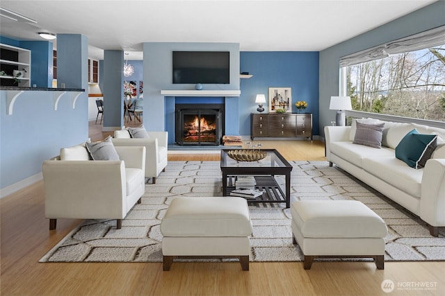 living room featuring a warm lit fireplace, light wood-style flooring, and baseboards