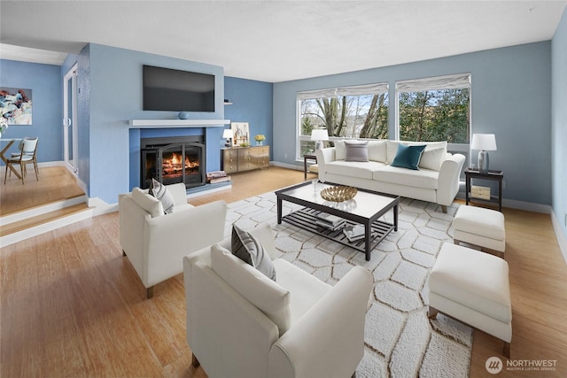 living area featuring a warm lit fireplace, light wood-style flooring, and baseboards