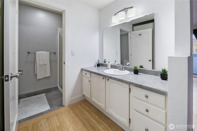 bathroom with a stall shower, vanity, baseboards, and wood finished floors