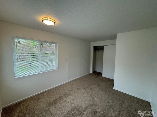 unfurnished bedroom featuring a textured ceiling, dark carpet, and a closet