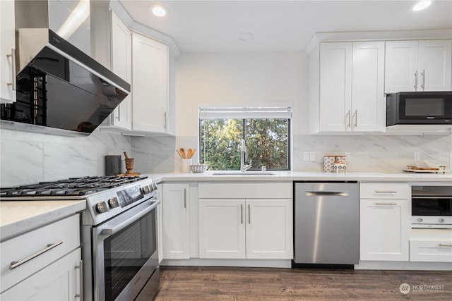 kitchen with tasteful backsplash, white cabinets, wall chimney range hood, sink, and stainless steel appliances