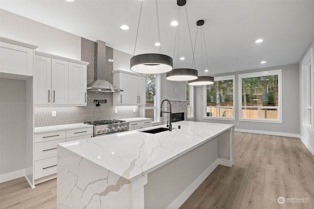 kitchen featuring sink, white cabinets, wall chimney range hood, and a large island