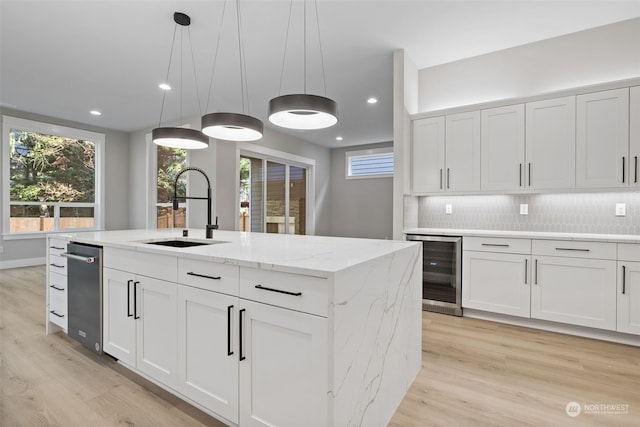 kitchen with tasteful backsplash, hanging light fixtures, a kitchen island with sink, sink, and white cabinets