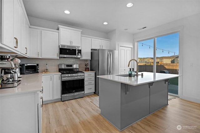 kitchen featuring light hardwood / wood-style flooring, sink, white cabinetry, a center island with sink, and stainless steel appliances