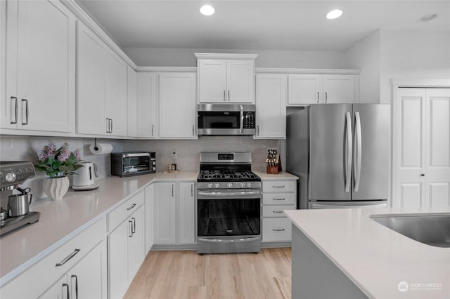 kitchen with white cabinets, appliances with stainless steel finishes, tasteful backsplash, sink, and light hardwood / wood-style flooring