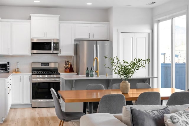 kitchen with light hardwood / wood-style floors, backsplash, white cabinetry, and appliances with stainless steel finishes