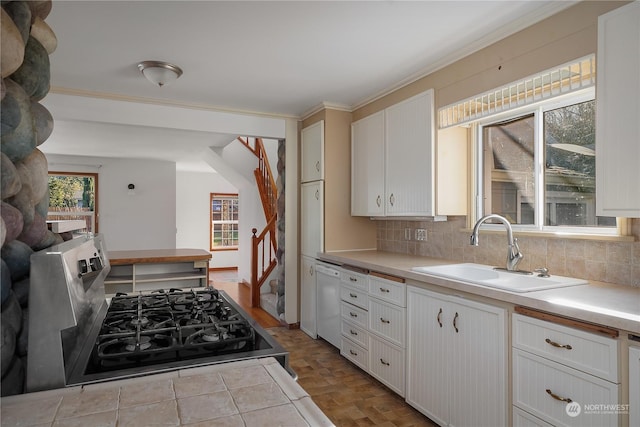 kitchen featuring white dishwasher, sink, backsplash, stainless steel stove, and white cabinets