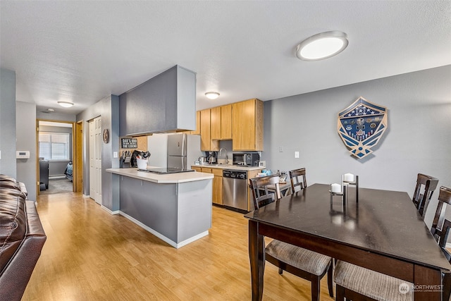 kitchen featuring light brown cabinetry, sink, light wood-type flooring, kitchen peninsula, and stainless steel appliances