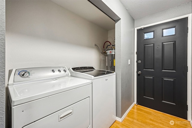 laundry room featuring electric water heater, a textured ceiling, washing machine and clothes dryer, and light hardwood / wood-style floors