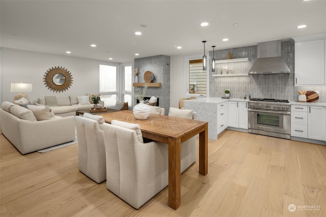 kitchen with pendant lighting, high end stainless steel range, white cabinets, tasteful backsplash, and wall chimney range hood