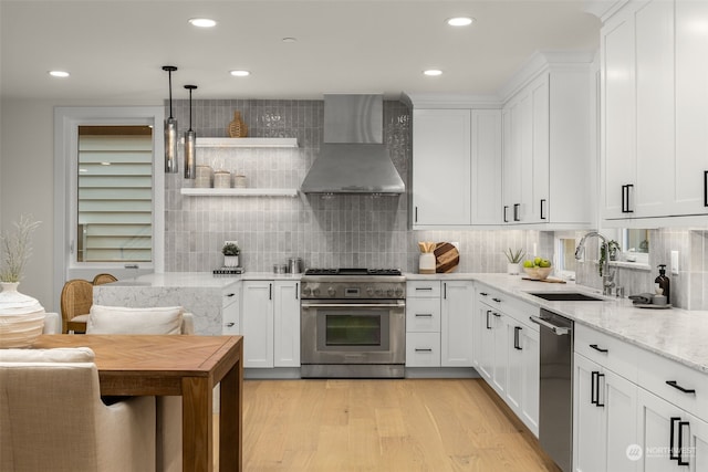 kitchen with appliances with stainless steel finishes, white cabinetry, wall chimney range hood, sink, and light stone counters