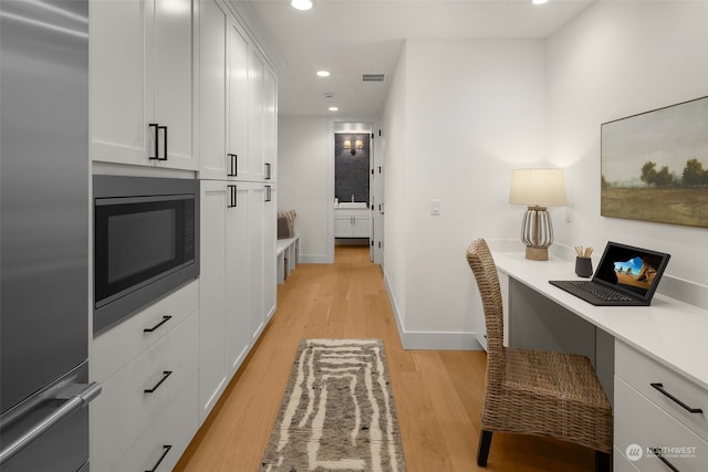 kitchen with white cabinets, light hardwood / wood-style flooring, built in appliances, and built in desk