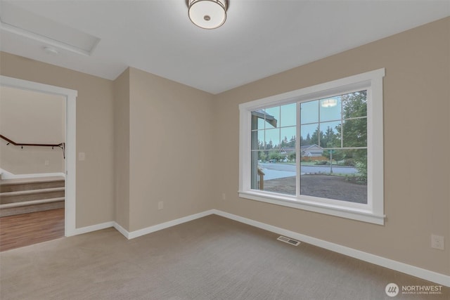 empty room featuring light colored carpet, visible vents, baseboards, and stairs