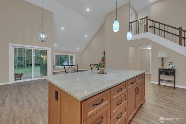 kitchen featuring light stone counters, hanging light fixtures, a kitchen island, light wood-type flooring, and baseboards