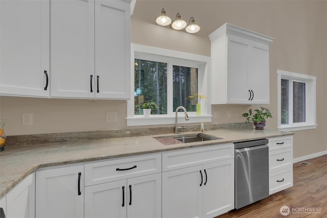 kitchen with white cabinets, dishwasher, light stone counters, wood finished floors, and a sink