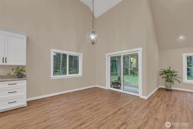 unfurnished living room with a chandelier, high vaulted ceiling, light wood-type flooring, and baseboards