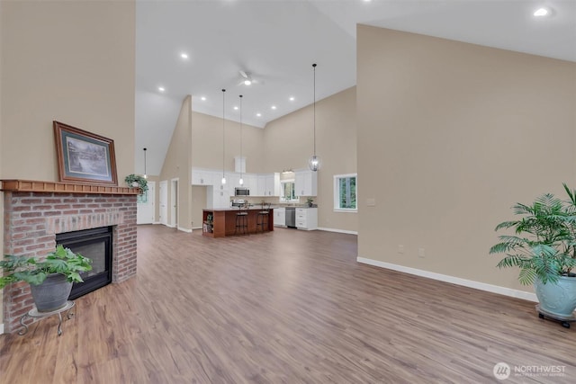 unfurnished living room featuring a fireplace, recessed lighting, a high ceiling, wood finished floors, and baseboards