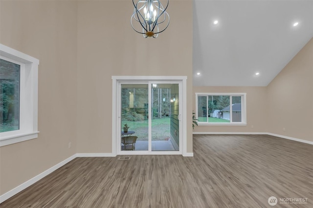 unfurnished living room featuring baseboards, wood finished floors, an inviting chandelier, high vaulted ceiling, and recessed lighting