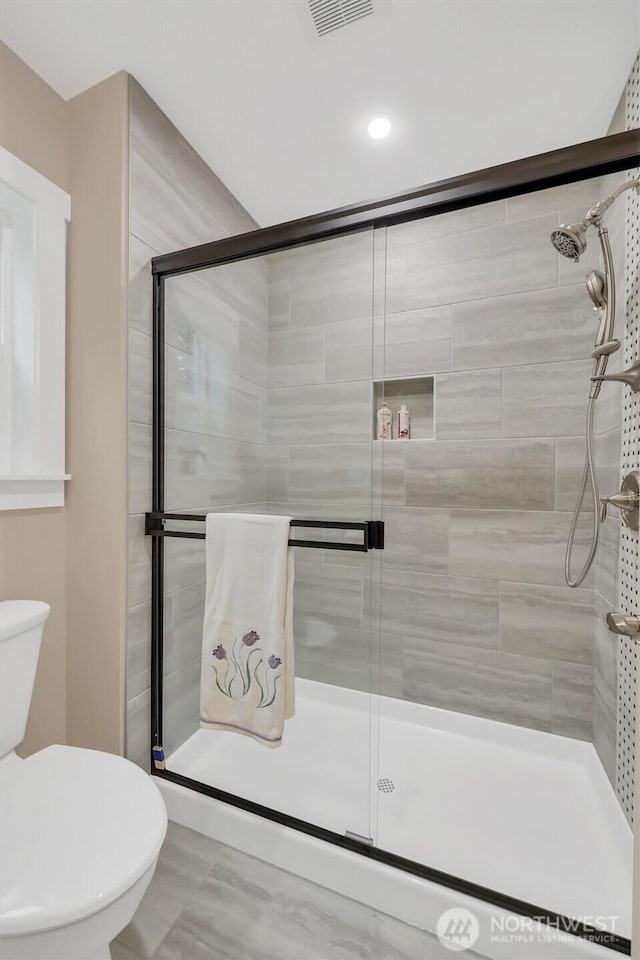 full bath with toilet, a stall shower, and visible vents