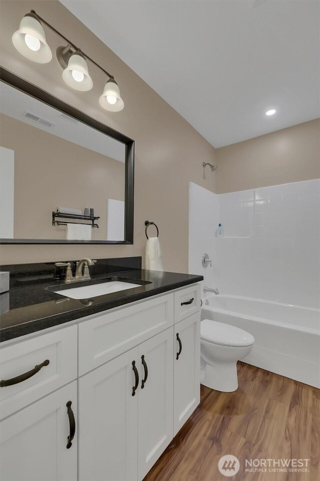 bathroom with toilet, wood finished floors, vanity, visible vents, and shower / bathing tub combination