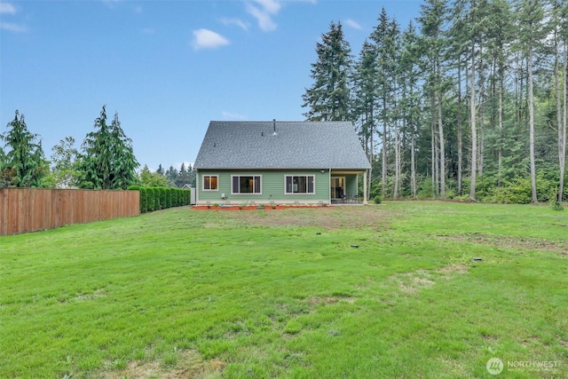 rear view of house featuring roof with shingles, a lawn, and fence