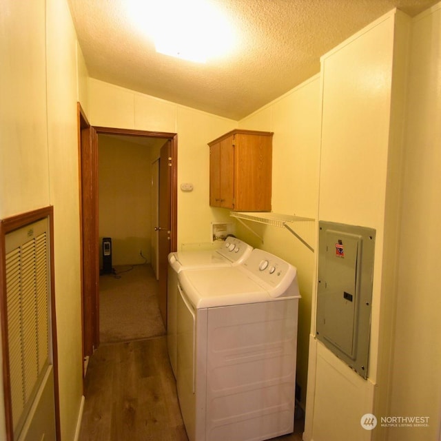 clothes washing area with a textured ceiling, cabinets, washing machine and clothes dryer, hardwood / wood-style flooring, and electric panel