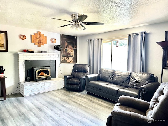 living room with a wood stove, ceiling fan, light hardwood / wood-style flooring, and a textured ceiling