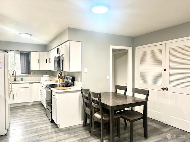 kitchen with sink, stainless steel appliances, white cabinetry, and light hardwood / wood-style floors