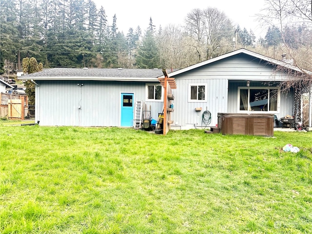 rear view of property with a hot tub and a lawn