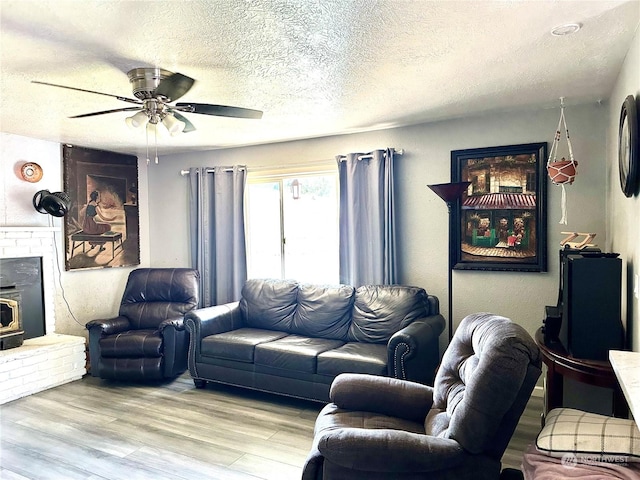 living room featuring a wood stove, ceiling fan, light hardwood / wood-style floors, and a textured ceiling