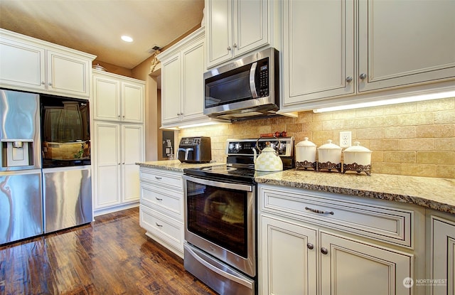 kitchen with dark hardwood / wood-style floors, stainless steel appliances, light stone countertops, decorative backsplash, and white cabinets