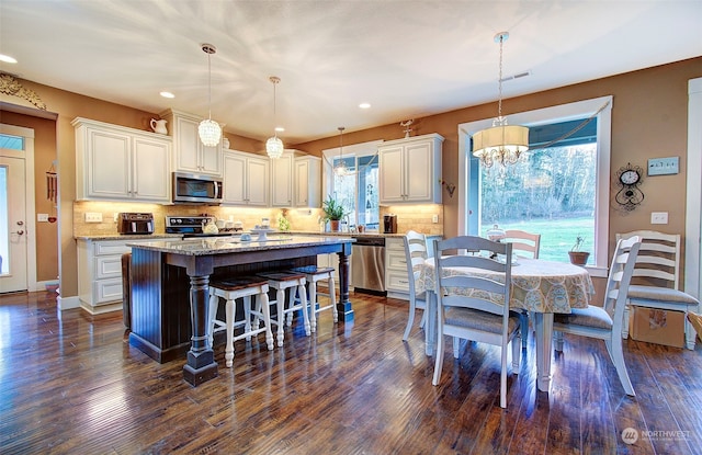 kitchen featuring white cabinetry, appliances with stainless steel finishes, a center island, and decorative light fixtures