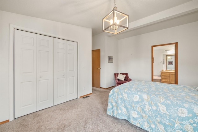 carpeted bedroom with ensuite bathroom, a closet, and a notable chandelier