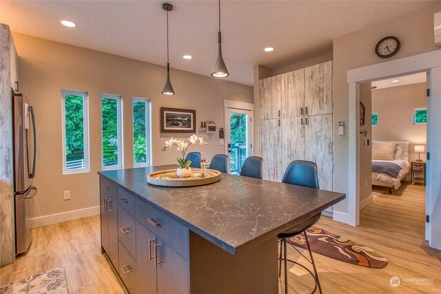 kitchen with a kitchen island, light wood-style flooring, freestanding refrigerator, dark countertops, and a wealth of natural light