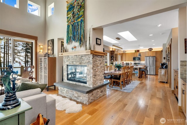 living area featuring light wood-type flooring, recessed lighting, a high ceiling, a skylight, and a multi sided fireplace