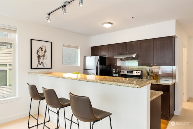 kitchen with decorative backsplash, light stone counters, appliances with stainless steel finishes, and a kitchen island