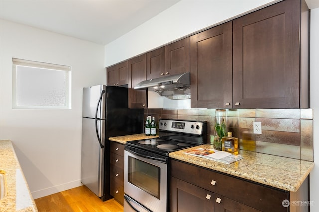 kitchen with dark brown cabinets, light hardwood / wood-style flooring, appliances with stainless steel finishes, backsplash, and light stone countertops